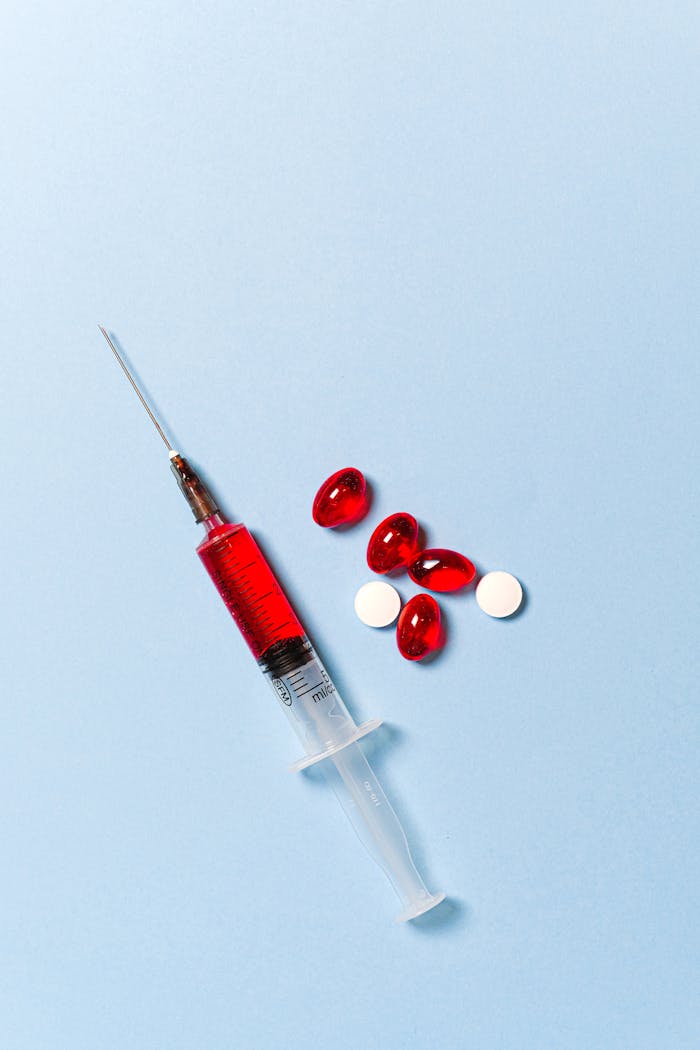Syringe with red liquid and pills on a blue backdrop symbolizing medical treatment.