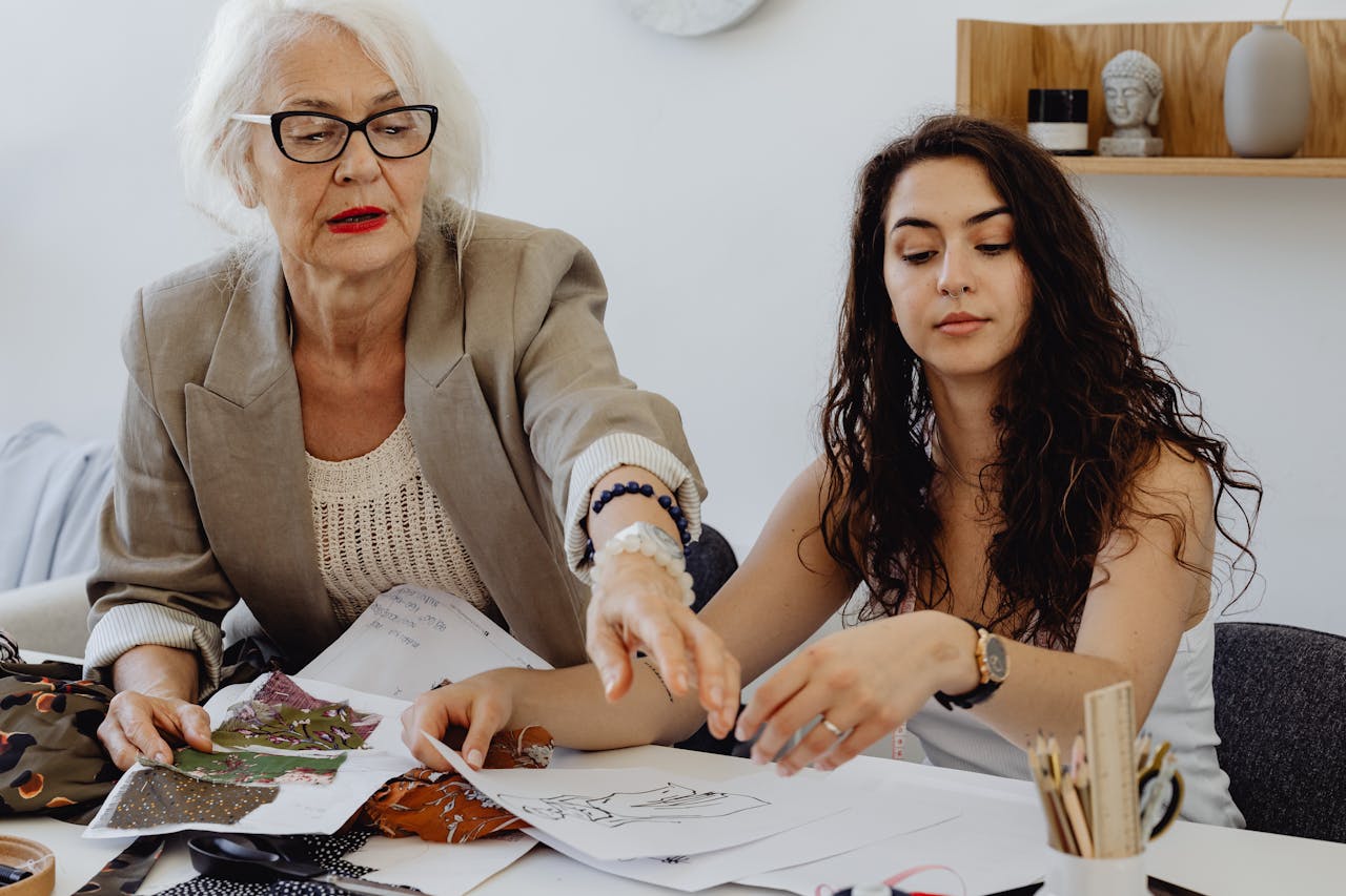 A senior woman and young woman collaborate on fashion designs indoors.